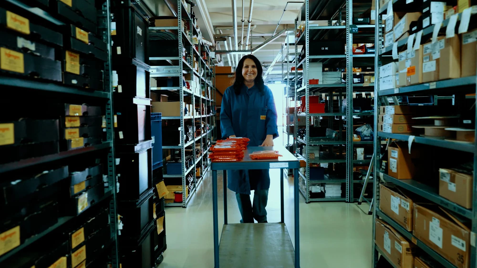 Frau in Laborkittel arbeitet an kleinen Elektronikteilen in einem High-Tech-Labor. Mikroskop und Roboterarm im Hintergrund.