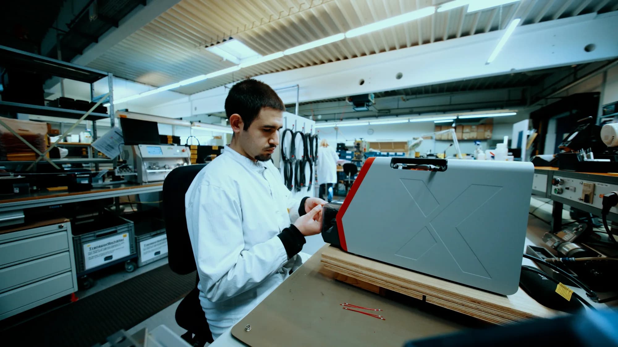 Blondes Haar, arbeitet bei der Elektronikfertigung in einer hellen Industriehalle; Vorne liegen SMD und THT Bestückung Materialien.
