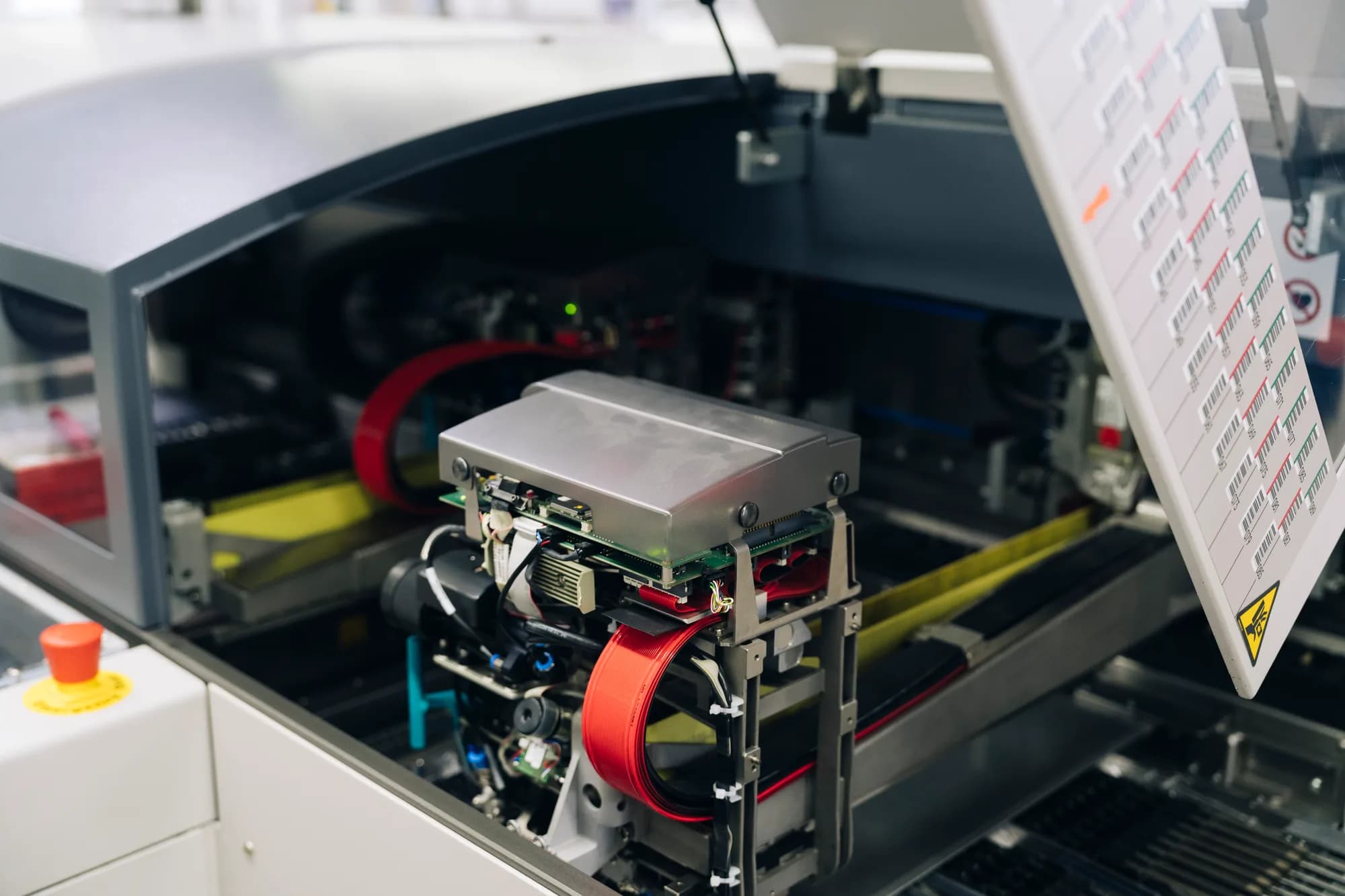 Detailaufnahme einer elektronischen Baugruppenfertigung: Silbere Mechanik, rotes Detail, komplexe Verkabelung und Datenblatt.