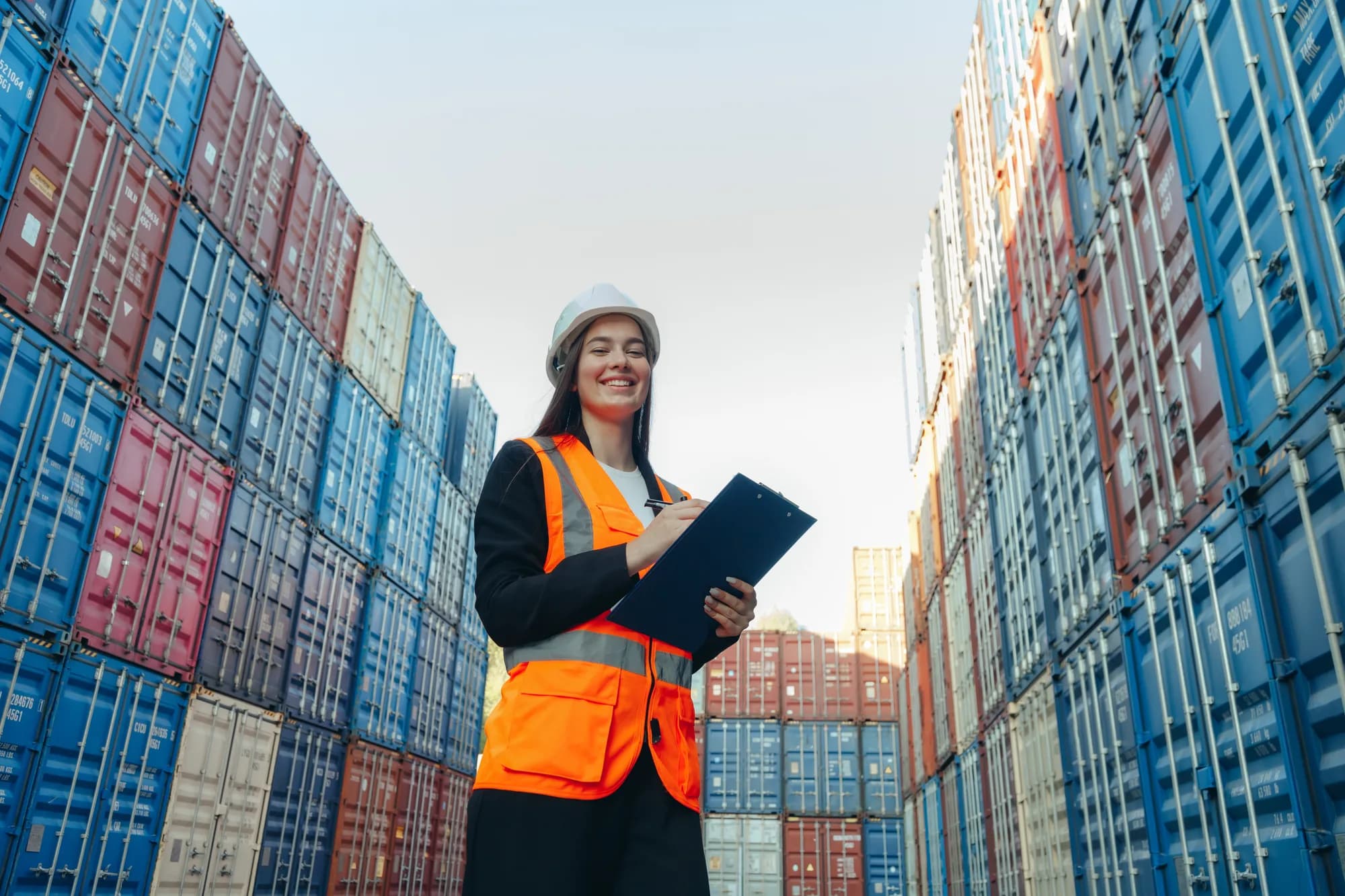 Ingenieurin mit Clipfolder in weißem Helm und Weste arbeitet im Containerterminalhafen