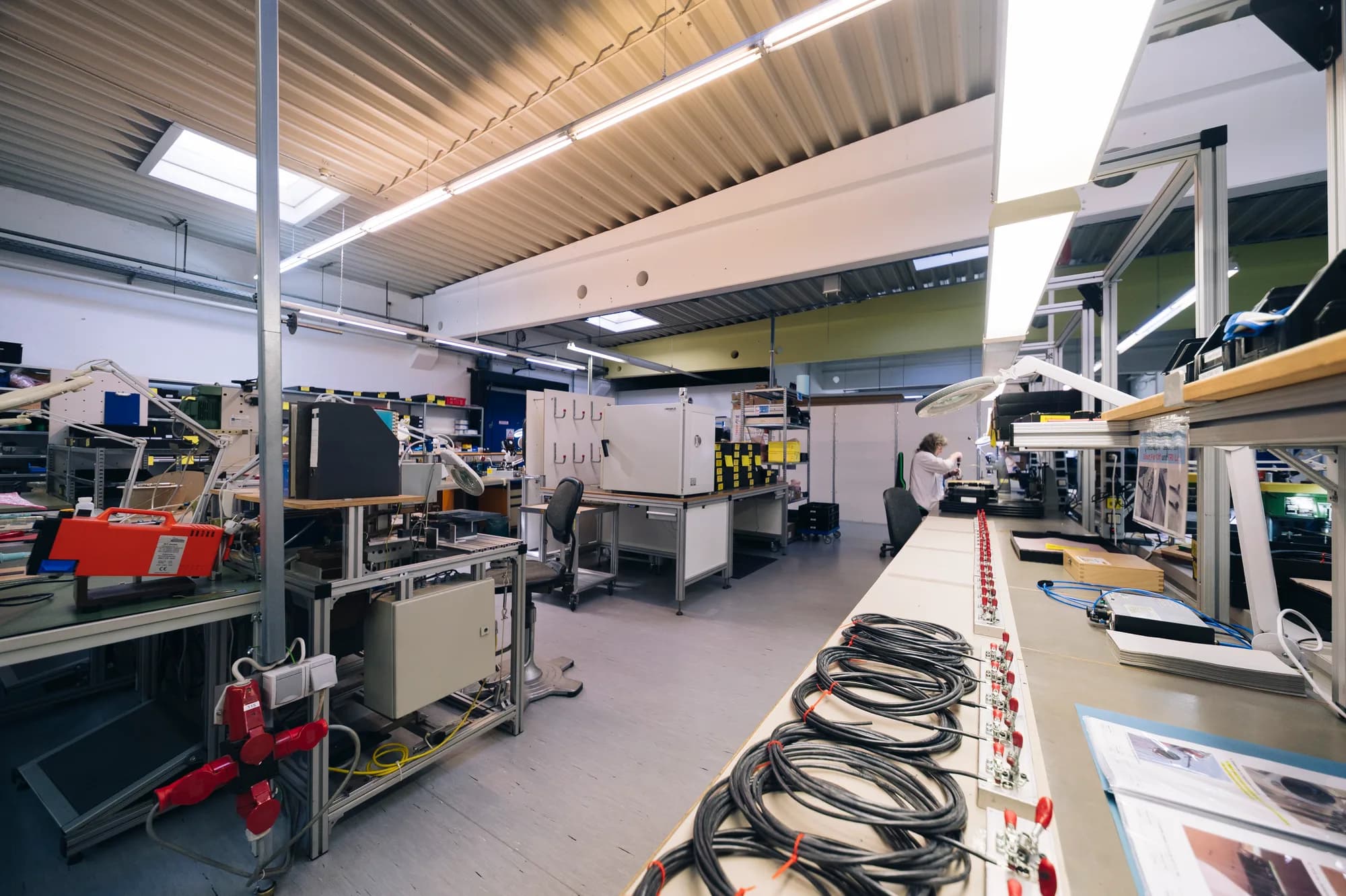 Technischer Arbeitsbereich zur Elektronikfertigung: Lange weiße Arbeitsfläche mit komplexen Kabelbäumen und elektronischen Modulen für Baugruppenfertigung Nürnberg.